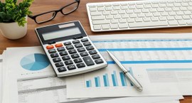 obre uma mesa de trabalho, há uma calculadora, um teclado de computador, uma caneta e documentos...