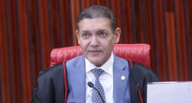 Presidente do TSE veste toga preta com detalhes vermelhos sobre terno azul-claro, camisa branca ...