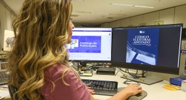 Mulher sentada ao computador olhando na tela o Código Eleitoral Anotado e Legislação Complementar