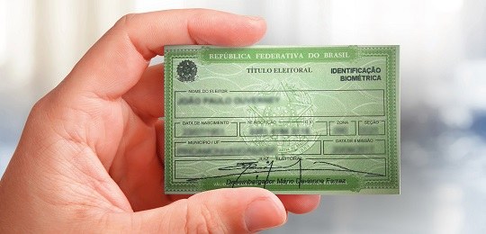 Fotografia da mão de uma pessoa segurando um título eleitoral impresso.