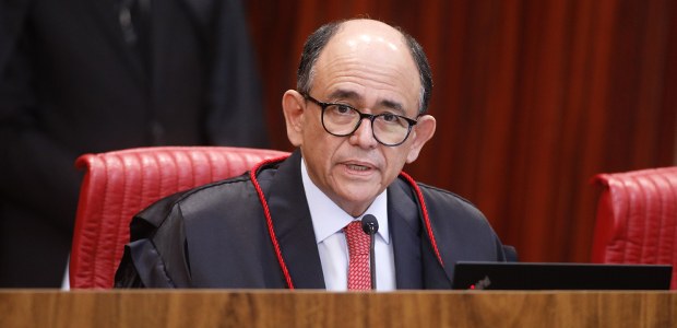 Foto de homem de pele clara e calvo, usando óculos, sentado em uma cadeira vermelha no plenário ...
