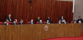 Plenário do TSE. Tem uma longa bancada de madeira ocupa o centro da imagem. Atrás dela os minist...