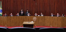 Plenario TSE.  Os ministros estão sentados atrás de uma longa bancada de madeira, todos vestidos...