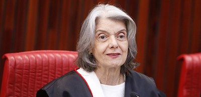 A imagem mostra a Ministra Cármen Lúcia, possui cabelos grisalhos, trajando uma toga preta com d...