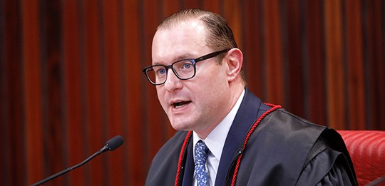 A imagem mostra o Ministro Cristiano Zanin, homem de óculos, com cabelo penteado para trás, usan...