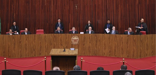 Fotografia em plano geral de um plenário formal com paredes revestidas de painéis de madeira ver...