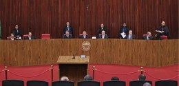 Fotografia em plano geral de um plenário formal com paredes revestidas de painéis de madeira ver...