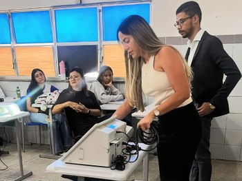 A imagem mostra um grupo de estudantes e adultos em uma sala de aula, participando de uma ativid...