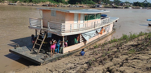 Fotografia mostra uma embarcação de madeira parada na margem de um rio de água barrenta. O barco...