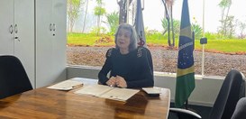 Ministra Cármen Lúcia participa de videoconferência. Está sentada atrás de uma mesa de madeira, ...