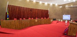 Plenário do TSE. Em primeiro plano e ao centro, há uma longa bancada de madeira em formato levem...