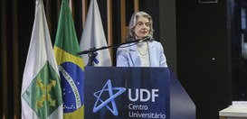 A imagem mostra a ministra Cármen Lúcia em pé, falando em um púlpito azul com o logotipo e o nom...