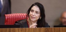 Estela Aranha em uma sessão plenária. Ela veste uma toga preta com detalhes em vermelho.