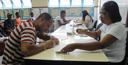 Imagem de eleitor assinando documentos e recebendo título de eleitor