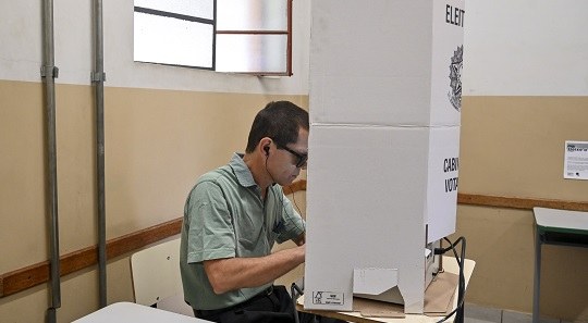 Homem com deficiência visual usa um fone de ouvido na cabine de votação