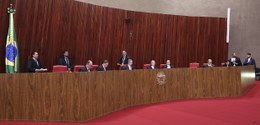 A imagem mostra o plenário do Tribunal Superior Eleitoral. Com uma longa bancada de madeira em f...