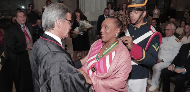 TRE-RJ homenageia personalidades que contribuíram para a democracia O presidente do Tribunal, de toga, cumprimenta a ministra Vera Lúcia, de roupa rosa. Um militar,...